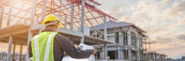 Professional engineer architect worker with protective helmet and blueprints paper at house building construction site background