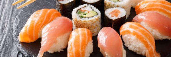 set of sushi and rolls with salmon and tuna, avocado, california, maki, soy sauce, chopsticks close-up on a black stone board on a table. horizontal