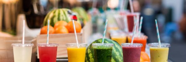 Close up color image depicting freshly made fruit juices and smoothies on display in a row and for sale at a food and drink market in London, UK. Selective focus on the plastic cups containing the fresh smoothies. In the background people are blurred out of focus. Room for copy space.