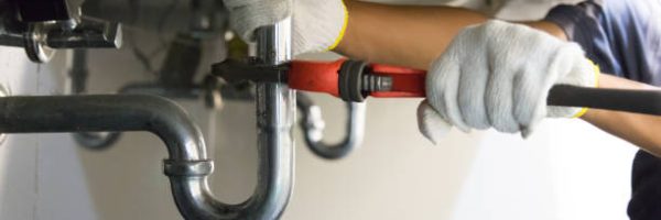 Plumber fixing white sink pipe with adjustable wrench.