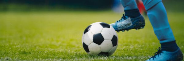 Close up of legs and feet of football player in blue socks and shoes running and dribbling with the ball. Soccer player running after the ball. Sports venue in the background