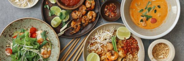 Authentic classic Pad Thai with shrimps. Thai shrimp satay with sweet chili sauce. Tom Yum soup with coconut milk (Tom Khaa). Spicy shrimp salad. Flat lay top-down composition on concrete background.