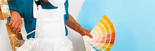 portrait of painter man with paintroller and wooden vintage ladder showing a color palette, on half painted wall