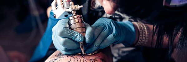 Close up tattoo artist demonstrates the process of getting black tattoo with paint. Master works in black sterile gloves. Master of tattoo fill circuit tattoo.