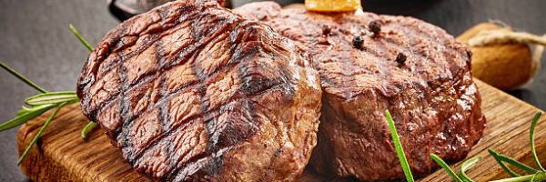 grilled beef steaks with spices on wooden cutting board