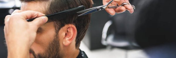 Close up of hairdresser arms cutting and combing male hair